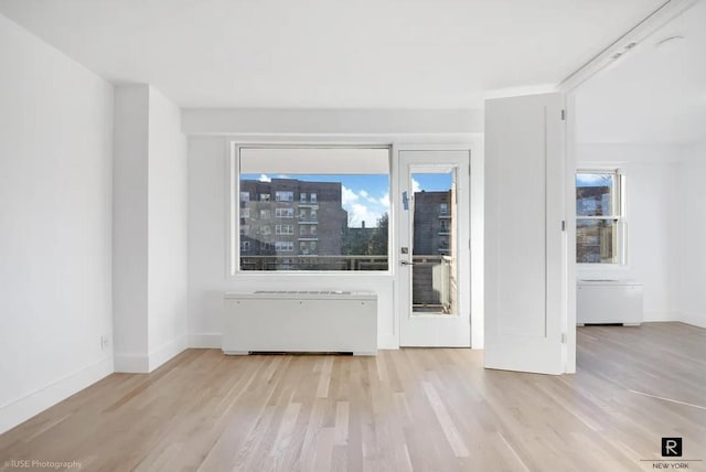 spare room featuring radiator heating unit, baseboards, and light wood finished floors