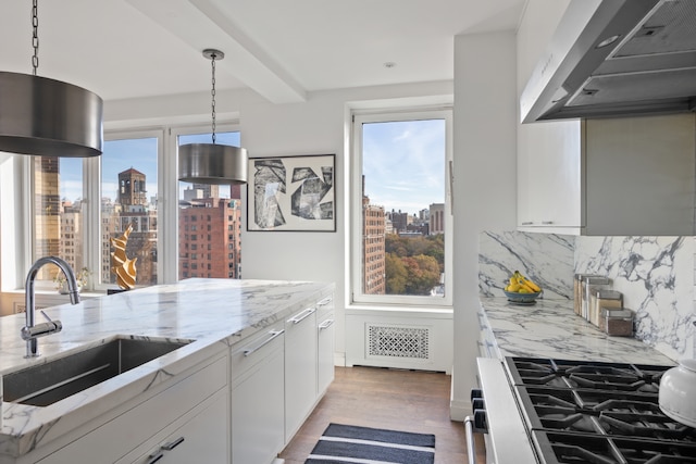 kitchen featuring pendant lighting, wall chimney range hood, sink, light stone counters, and white cabinets