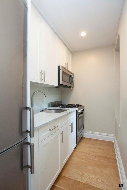 kitchen featuring white cabinets, light wood-type flooring, stainless steel appliances, and a sink