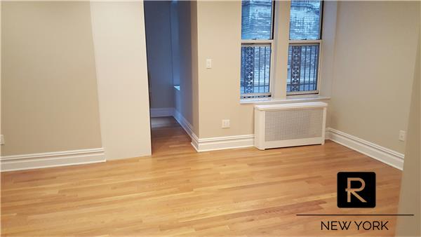 spare room with baseboards, wood finished floors, and radiator