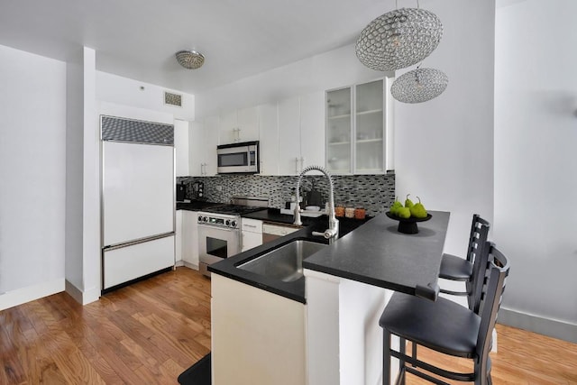 kitchen featuring pendant lighting, hardwood / wood-style floors, white cabinetry, sink, and high quality appliances