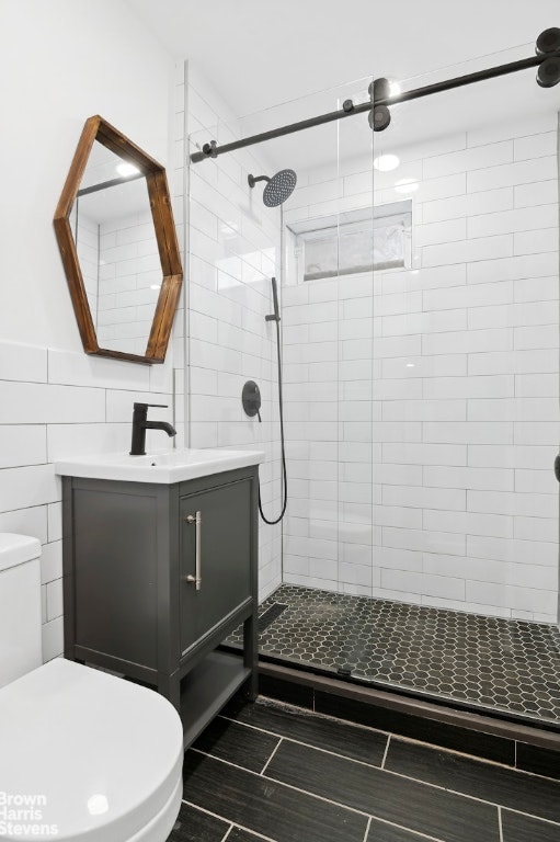 bathroom featuring vanity, toilet, tile walls, and a tile shower