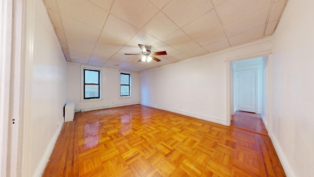 unfurnished room with a drop ceiling, a ceiling fan, radiator heating unit, and baseboards