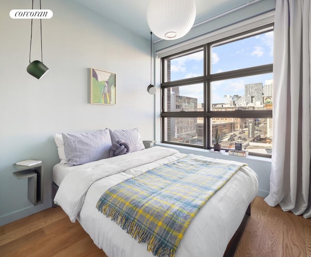 bedroom with a view of city and wood finished floors