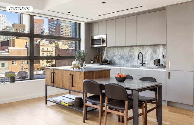 kitchen with a sink, light wood-style floors, a city view, stainless steel microwave, and backsplash