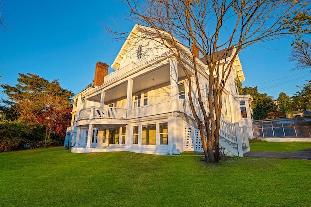 rear view of house featuring a balcony and a lawn