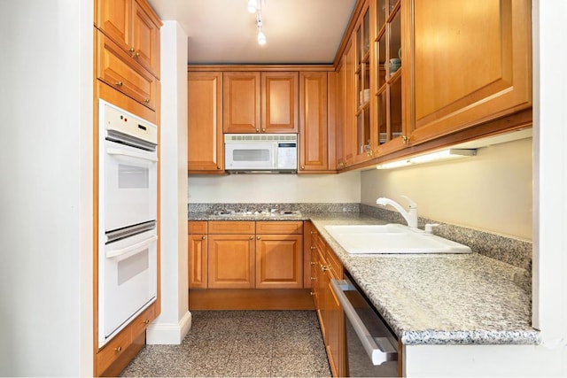 kitchen featuring rail lighting, light stone countertops, sink, and white appliances