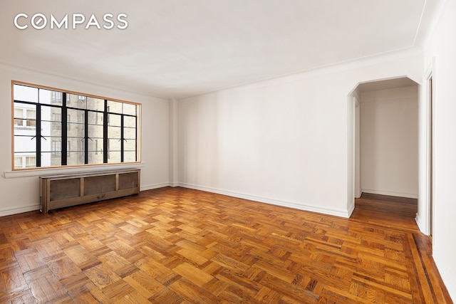 empty room featuring radiator, arched walkways, and baseboards