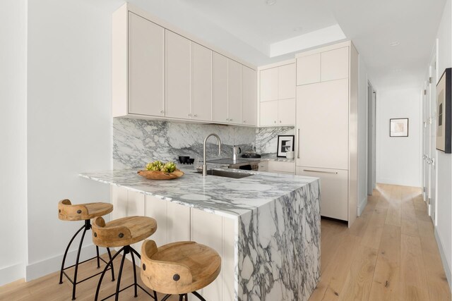 kitchen with backsplash, light stone countertops, a sink, a breakfast bar, and light wood-style flooring