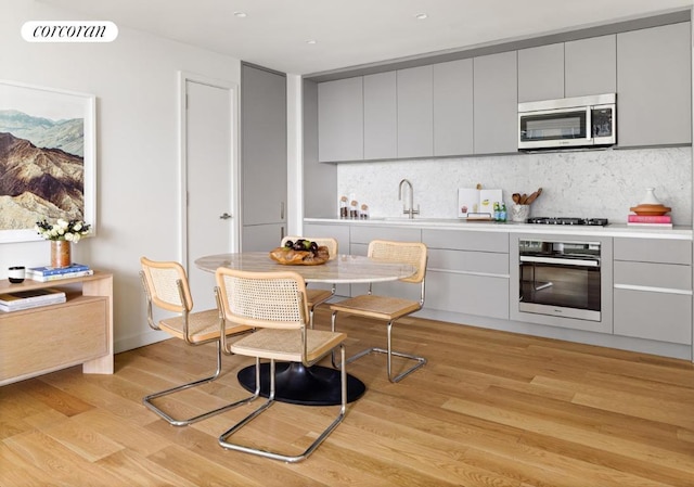 kitchen featuring sink, tasteful backsplash, gray cabinets, stainless steel appliances, and light hardwood / wood-style floors