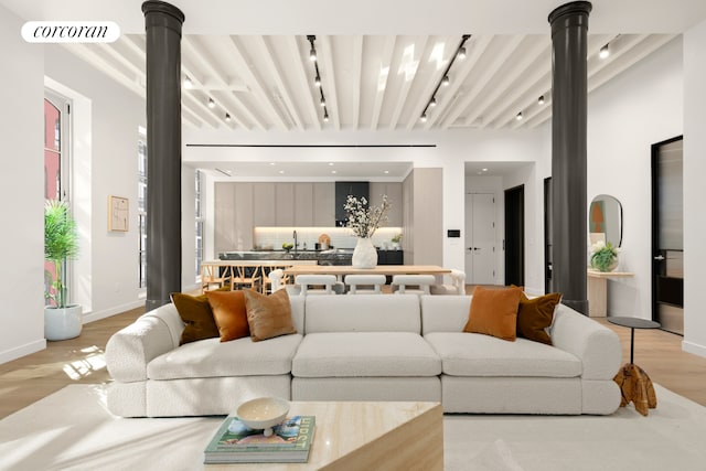 living area with light wood-type flooring, baseboards, rail lighting, and ornate columns