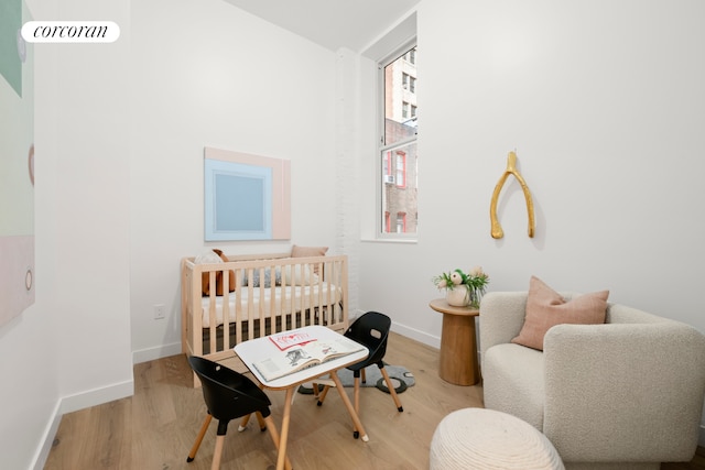 bedroom with a nursery area, wood finished floors, and baseboards