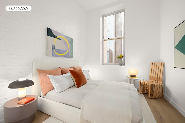 bedroom with visible vents, wood finished floors, baseboards, and brick wall