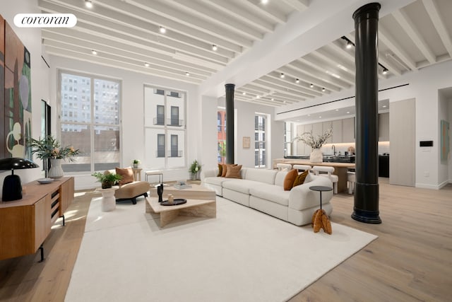 living room with beam ceiling, light wood finished floors, and decorative columns