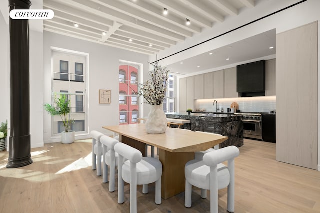 dining space featuring light wood finished floors and beamed ceiling