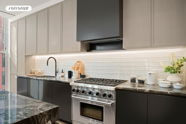 kitchen with a sink, dark stone counters, backsplash, and high end stove