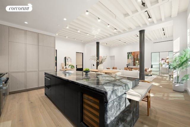 kitchen with light wood-style floors, a spacious island, dark stone counters, rail lighting, and beamed ceiling