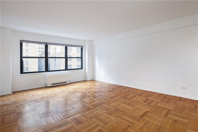 empty room with light parquet flooring and radiator