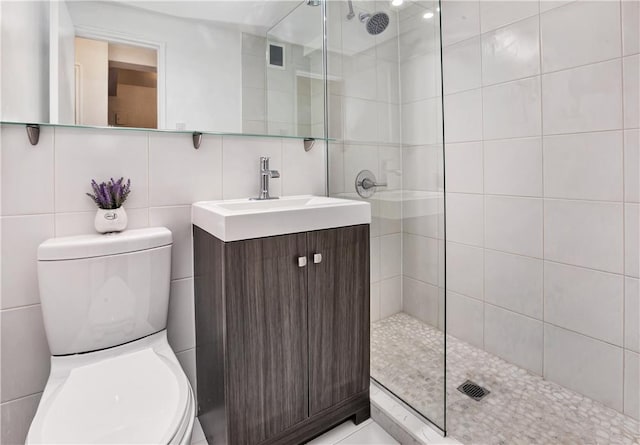 bathroom with tile walls, backsplash, vanity, tiled shower, and toilet