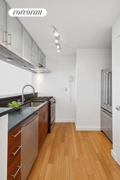 kitchen featuring a sink, baseboards, appliances with stainless steel finishes, light wood-type flooring, and dark countertops