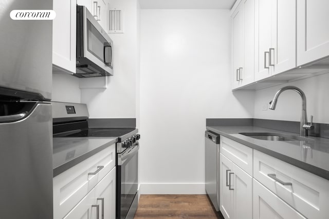 kitchen featuring white cabinets, dark countertops, dark wood-style flooring, stainless steel appliances, and a sink