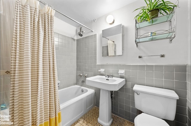 full bath with tile walls, toilet, shower / tub combo, wainscoting, and a sink