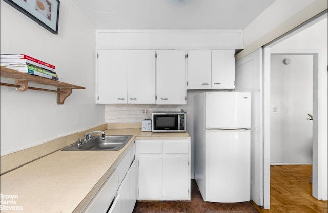 kitchen featuring stainless steel microwave, freestanding refrigerator, light countertops, white cabinetry, and a sink