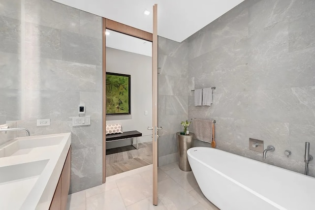 full bath with a freestanding bath, tile walls, a sink, and double vanity