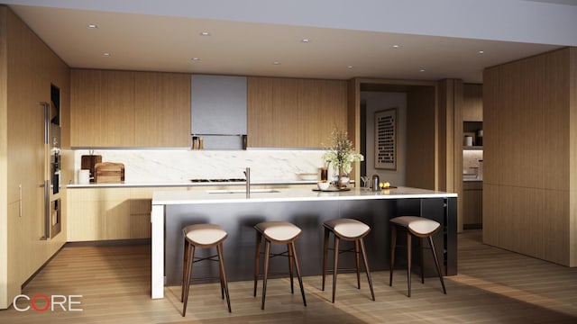 kitchen with light brown cabinetry, wall chimney range hood, a kitchen bar, and a center island with sink