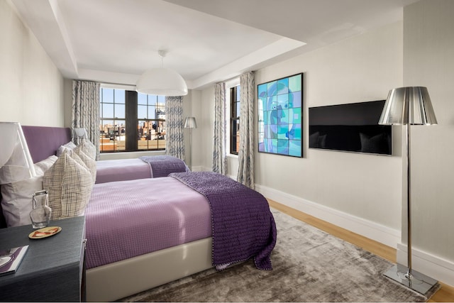 bedroom with a tray ceiling, wood finished floors, and baseboards