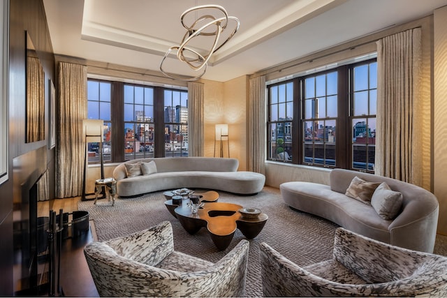 living room with a healthy amount of sunlight, a raised ceiling, and a notable chandelier