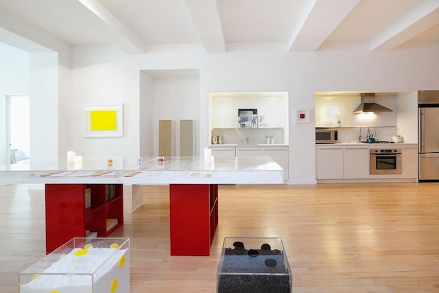 kitchen featuring light wood-style flooring, a kitchen island, appliances with stainless steel finishes, wall chimney exhaust hood, and beamed ceiling