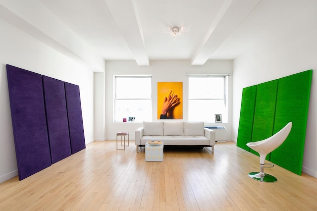 living area featuring baseboards, beam ceiling, a healthy amount of sunlight, and wood-type flooring