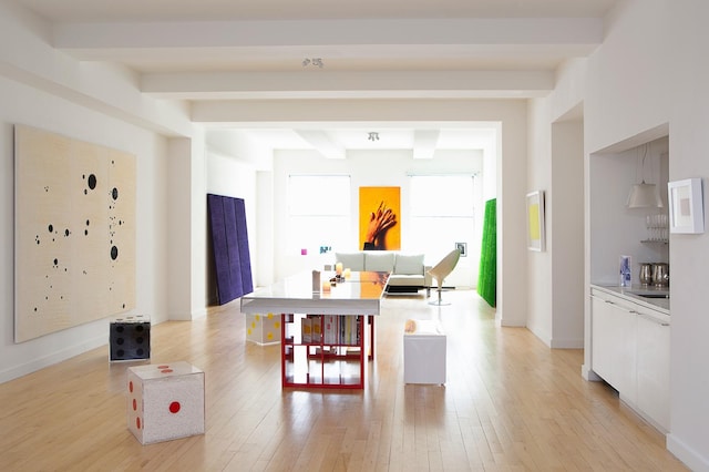 interior space featuring light wood-type flooring, beamed ceiling, modern cabinets, white cabinetry, and baseboards