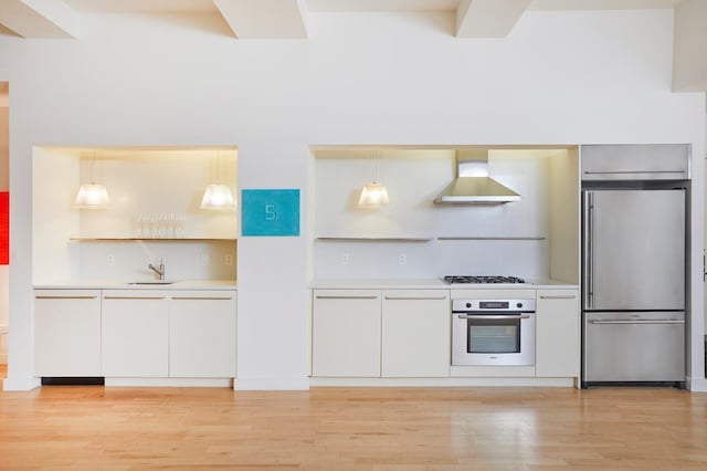 kitchen featuring light wood finished floors, wall chimney range hood, light countertops, appliances with stainless steel finishes, and a sink