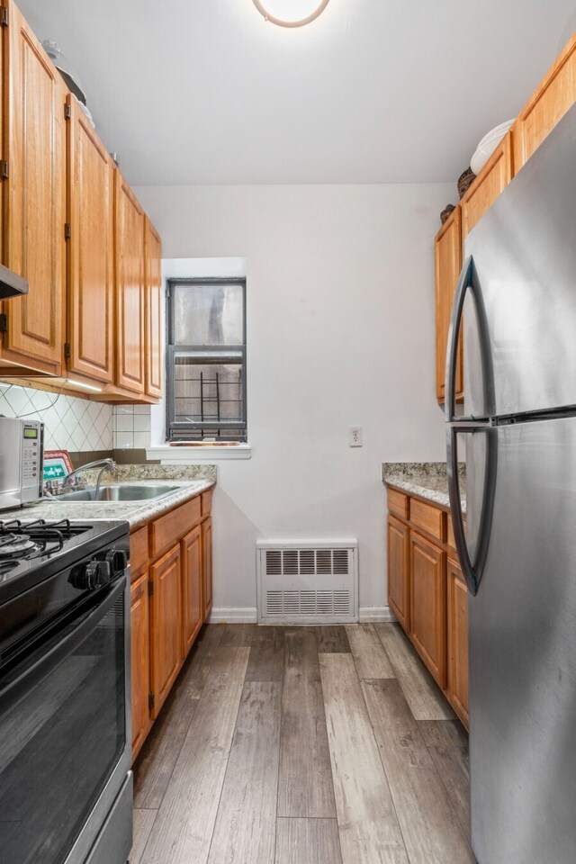 kitchen featuring sink, backsplash, stainless steel appliances, and light wood-type flooring