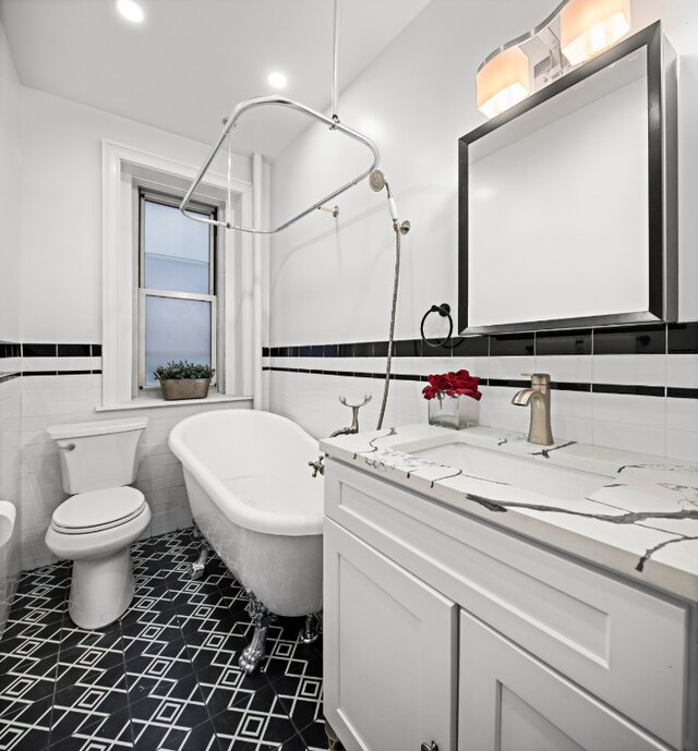 bathroom featuring a washtub, toilet, vanity, and tile walls