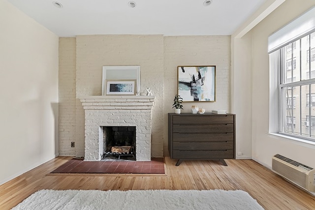 interior space featuring a brick fireplace, baseboards, wood finished floors, and a wall mounted air conditioner