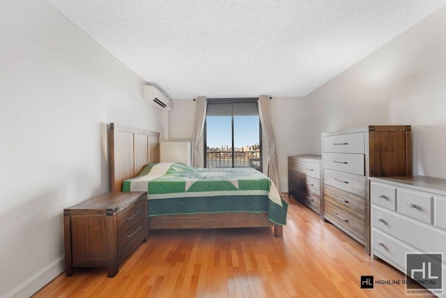 bedroom with light wood-style floors, a wall mounted air conditioner, a textured ceiling, and baseboards