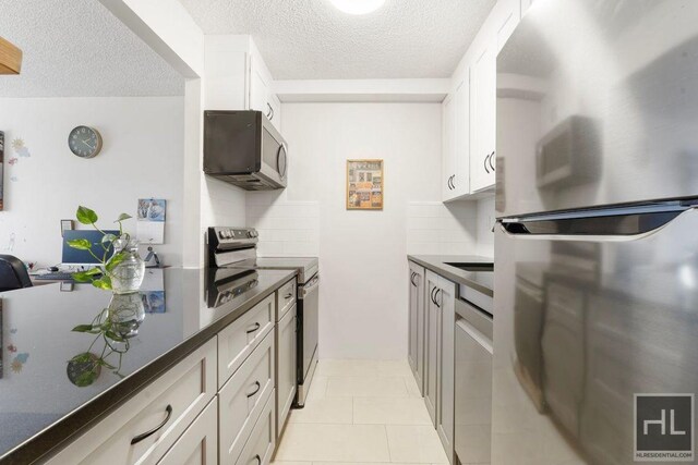 kitchen with stainless steel appliances, light tile patterned flooring, backsplash, and white cabinetry