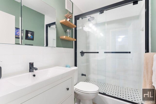 bathroom with toilet, vanity, tile walls, and a shower stall