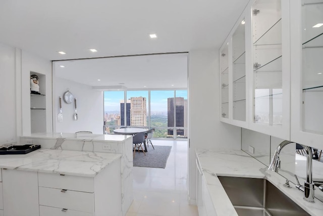 kitchen with floor to ceiling windows, white cabinets, light stone counters, and sink