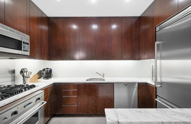 kitchen featuring light tile patterned floors, appliances with stainless steel finishes, light stone counters, dark brown cabinetry, and sink