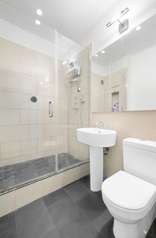 bathroom featuring toilet, tile walls, tile patterned flooring, sink, and a shower with door