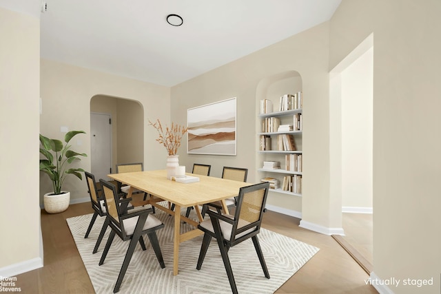 dining space with baseboards, light wood-style flooring, arched walkways, and built in features