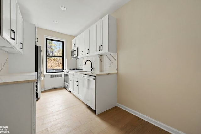 kitchen with radiator heating unit, white cabinetry, stainless steel appliances, sink, and light wood-type flooring