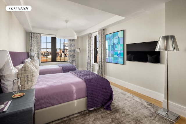 bedroom with a tray ceiling, wood finished floors, visible vents, and baseboards