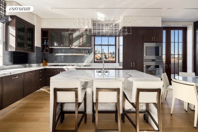 kitchen featuring light wood finished floors, tasteful backsplash, glass insert cabinets, a breakfast bar area, and double oven