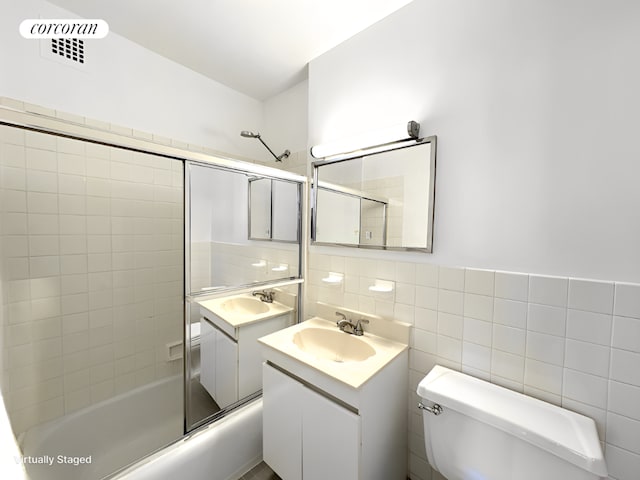 full bathroom featuring bath / shower combo with glass door, tile walls, vanity, and toilet