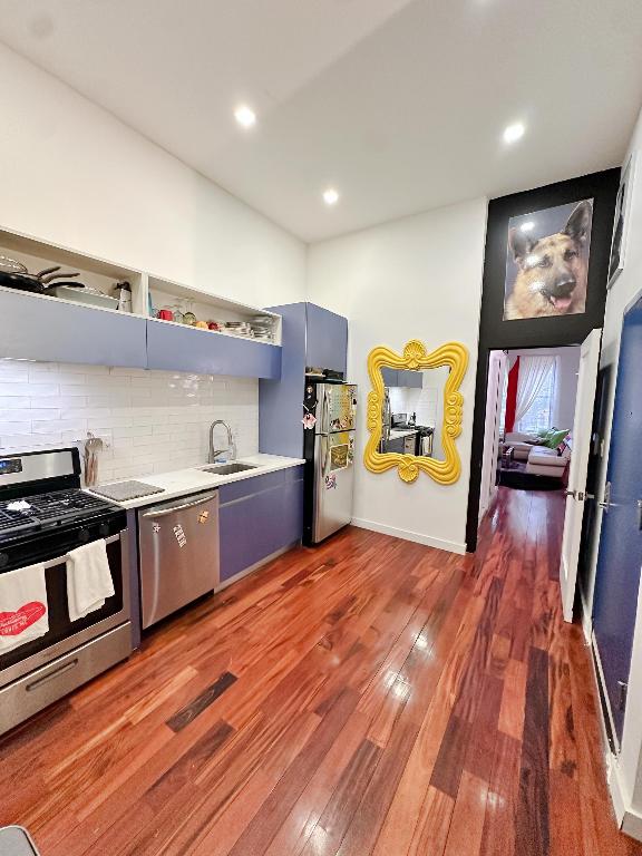 kitchen featuring dark hardwood / wood-style floors, decorative backsplash, sink, stainless steel appliances, and blue cabinets